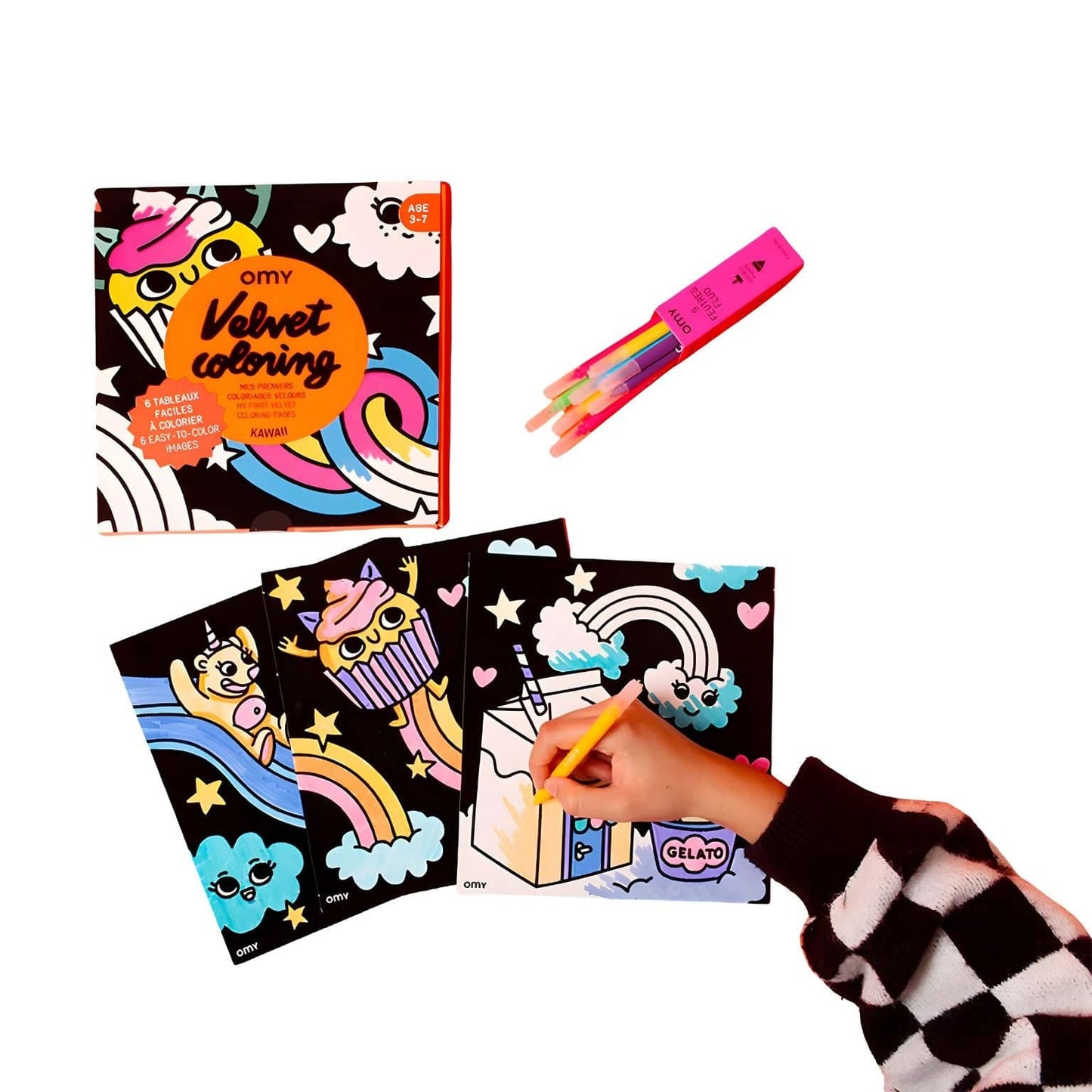 Criança a colorir o Livro colorir em veludo Lily da Omy com ilustrações kawaii, nuvens, arco-íris e cupcake sobre fundo colorido.