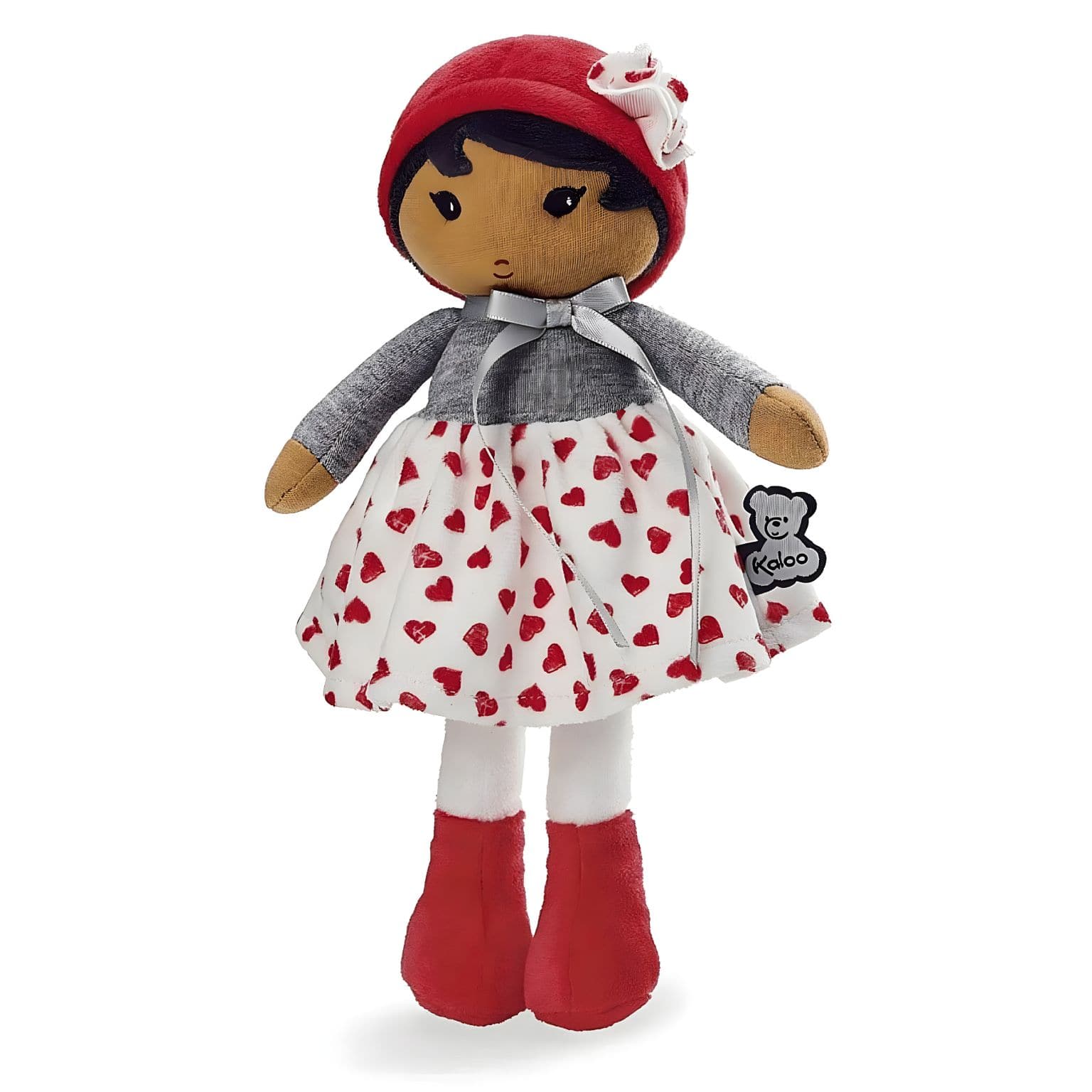 Boneca de Pano Jade da Kaloo com vestido branco de corações vermelhos, camisola cinzenta e gorro vermelho