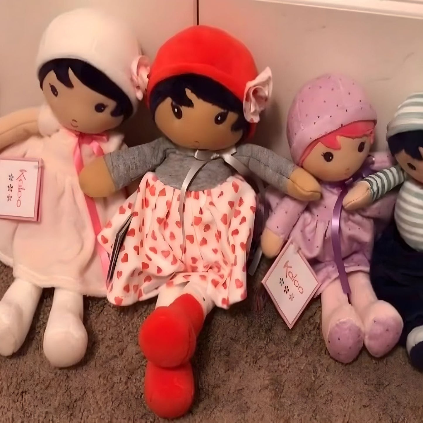 Boneca de Pano Jade da Kaloo com vestido branco de corações vermelhos, camisola cinzenta e gorro vermelho
