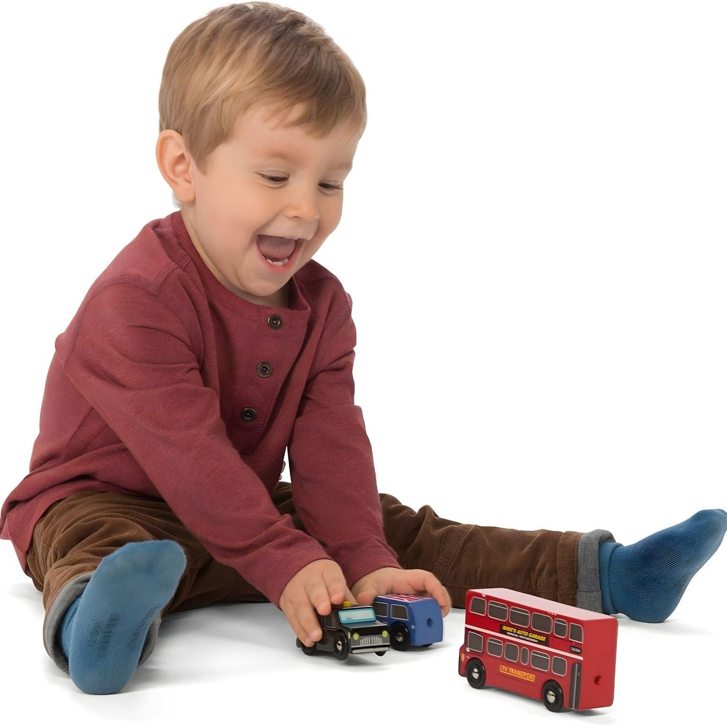 Criança a brincar com Conjunto Veículos de Londres em madeira da Le Toy Van com autocarro vermelho, táxi preto e carro azul