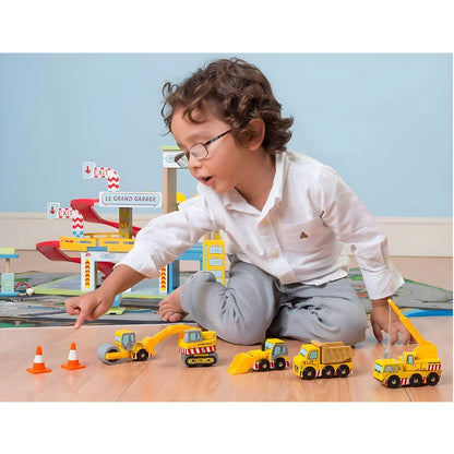 Child playing with Le Toy Van wooden construction vehicles, including truck, crane, excavator, loader, and cones.